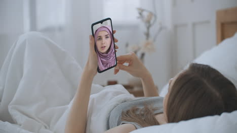 Frau-Nutzt-Medizinische-App-Auf-Dem-Smartphone-Und-Berät-Sich-Per-Videokonferenz-Mit-Einer-Arabischen-Muslimischen-Frau-Im-Hijab-Arzt.-Frau-Nutzt-Online-Chat,-Um-Mit-Familientherapeuten-Und-Einer-Coronavirus-Pandemie-Zu-Sprechen.